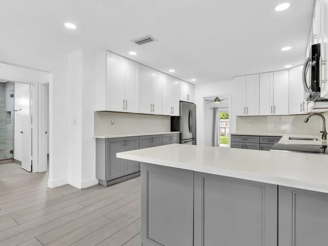 Kitchen featuring wood-finish vinyl flooring, two-tone cabinetry with white upper and grey lower units, stainless steel appliances, recessed lighting, and a white countertop