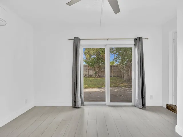 Bedroom with wood-finish ceiling fan with integrated lighting, and light grey vinyl flooring, sliding door exit to backyard