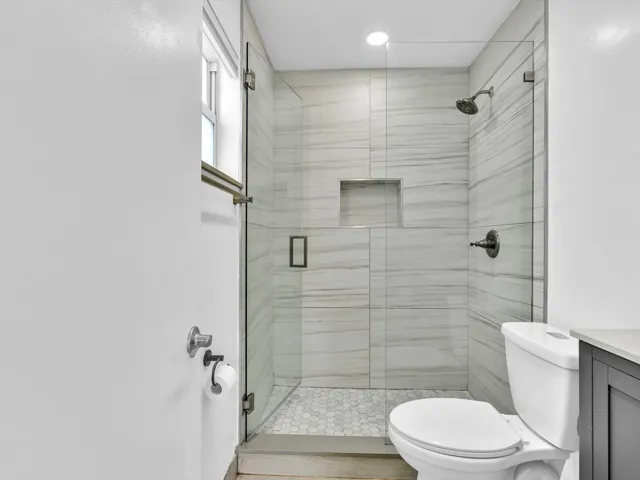 Primary Bedroom glass-enclosed shower with a recessed niche, hexagonal tile flooring, and horizontal tile walls
