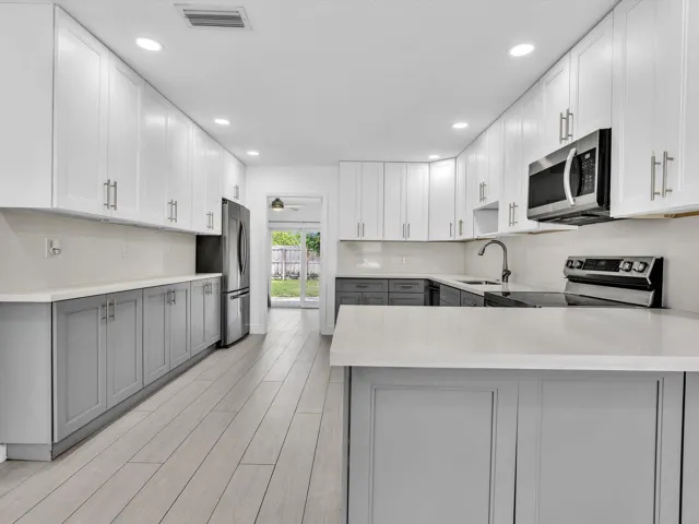 Kitchen featuring wood-finish vinyl flooring, two-tone cabinetry with white upper and grey lower units, stainless steel appliances, recessed lighting, and a white countertop