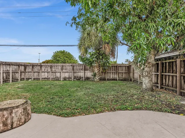 Private expansive fenced backyard featuring a concrete patio, wood fence, mature trees, and a grass lawn