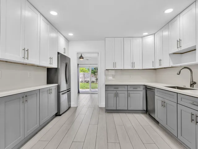 Kitchen featuring wood-finish vinyl flooring, two-tone cabinetry with white upper and grey lower units, stainless steel appliances, recessed lighting, and a white countertop