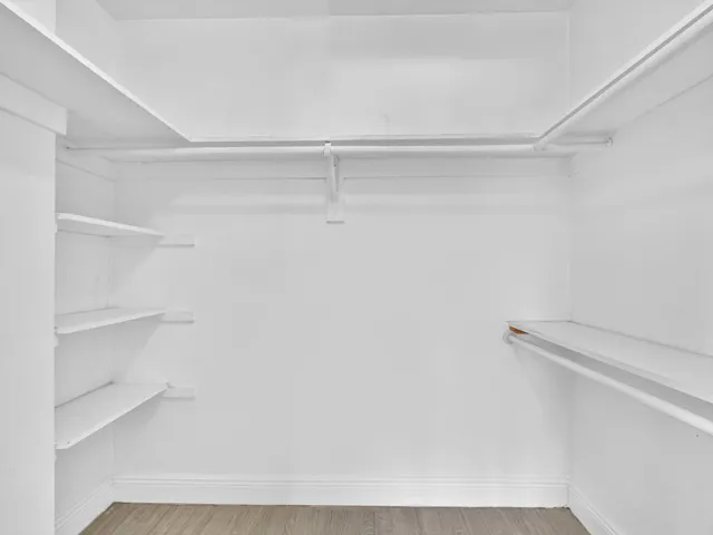 Primary Bedroom walk-in closet with multiple built-in shelves, integrated hanging rods, and wood-finish vinyl flooring
