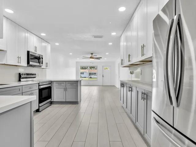 Kitchen featuring wood-finish vinyl flooring, two-tone cabinetry with white upper and grey lower units, stainless steel appliances, recessed lighting, and a white countertop