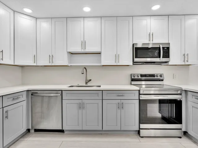 Kitchen featuring wood-finish vinyl flooring, two-tone cabinetry with white upper and grey lower units, stainless steel appliances, recessed lighting, and a white countertop