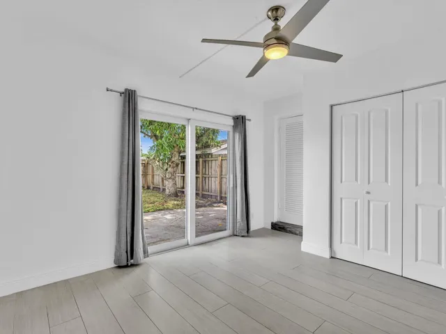Bedroom with wood-finish ceiling fan with integrated lighting, and light grey vinyl flooring, sliding door exit to backyard