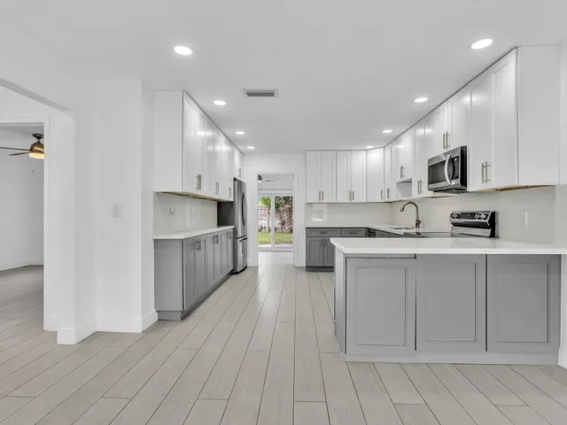 Kitchen featuring wood-finish vinyl flooring, two-tone cabinetry with white upper and grey lower units, stainless steel appliances, recessed lighting, and a white countertop
