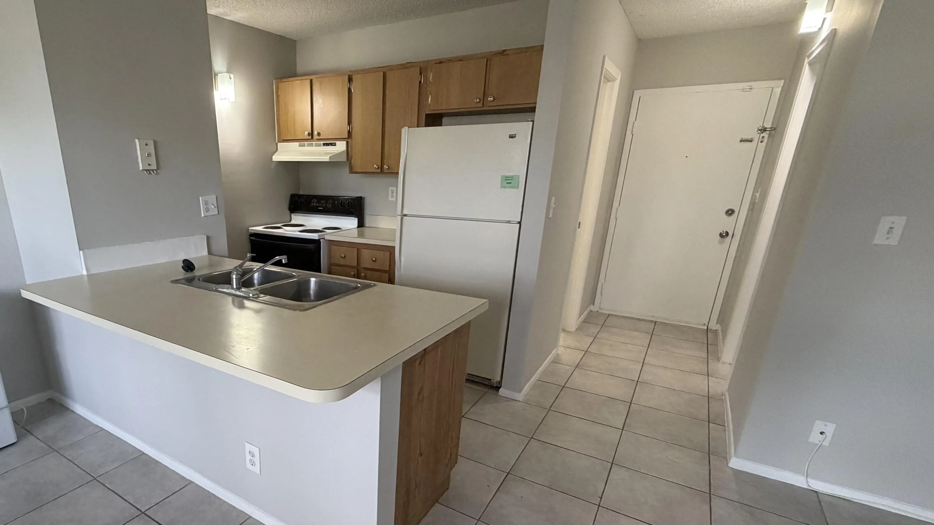 Kitchen featuring a breakfast bar with an integrated double basin sink, wood-finish cabinetry, white appliances, and a tile floor throughout the space