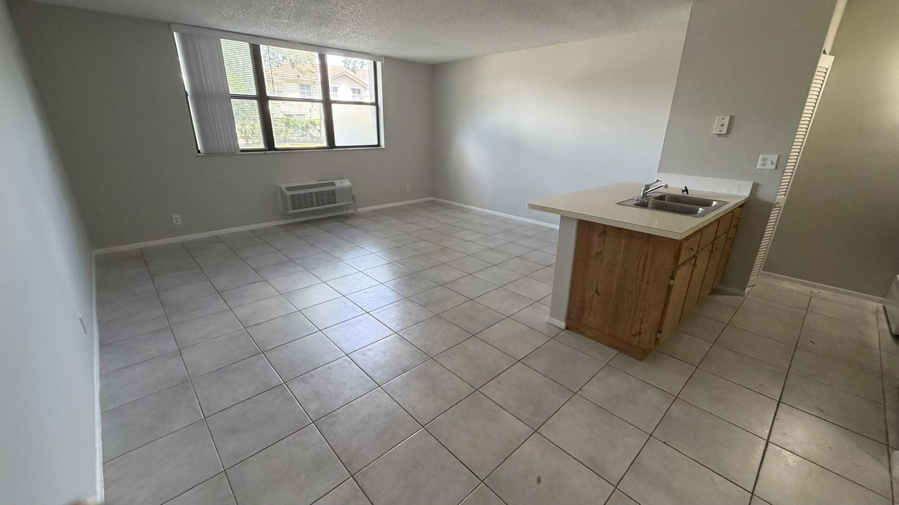 Tile flooring, large windows, wood-finish cabinetry, countertop with integrated double basin sink, and an wall-mounted air conditioning unit