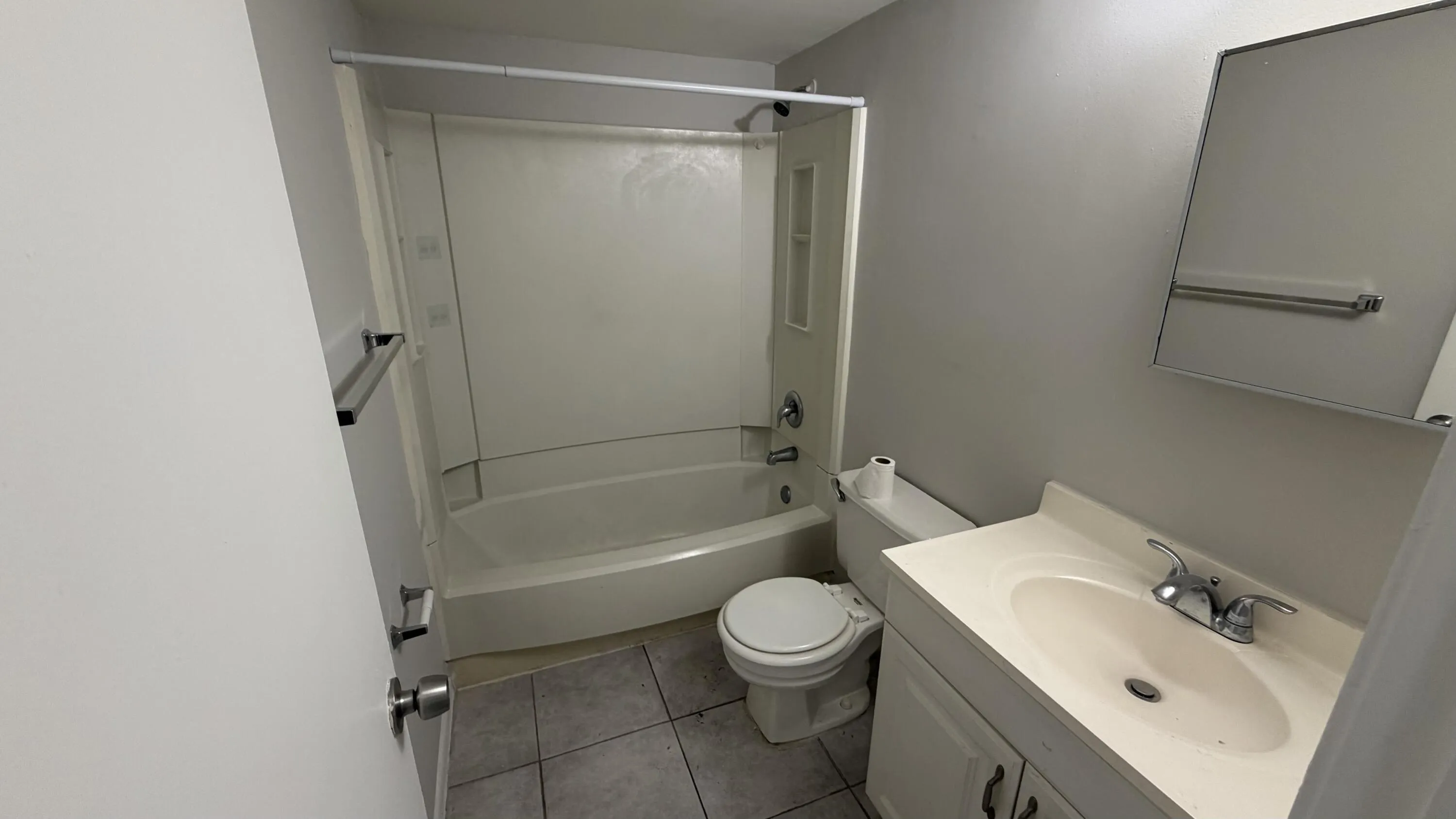 Full bathroom featuring a white tub/shower combination, a vanity with an integrated sink, a wall-mounted mirror, and tile flooring