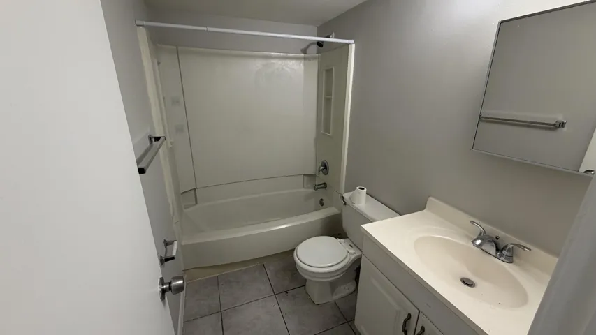 Full bathroom featuring a white tub/shower combination, a vanity with an integrated sink, a wall-mounted mirror, and tile flooring