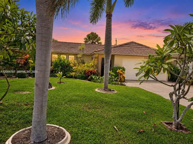 Single-story exterior featuring a concrete tile roof, attached garage, manicured lawn, and mature palm landscaping