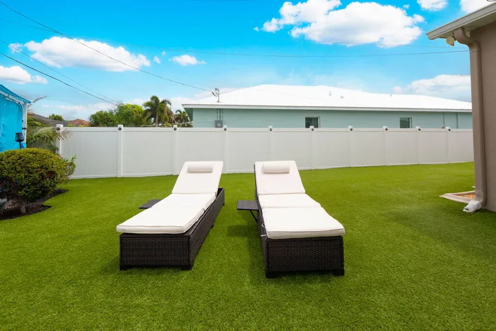 Turf backyard with lounge chairs and white privacy fence