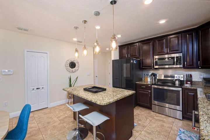 Kitchen featuring dark wood-finish cabinetry, stainless steel appliances, a center island with a stone-finish countertop, pendant lighting, and ceramic tile flooring