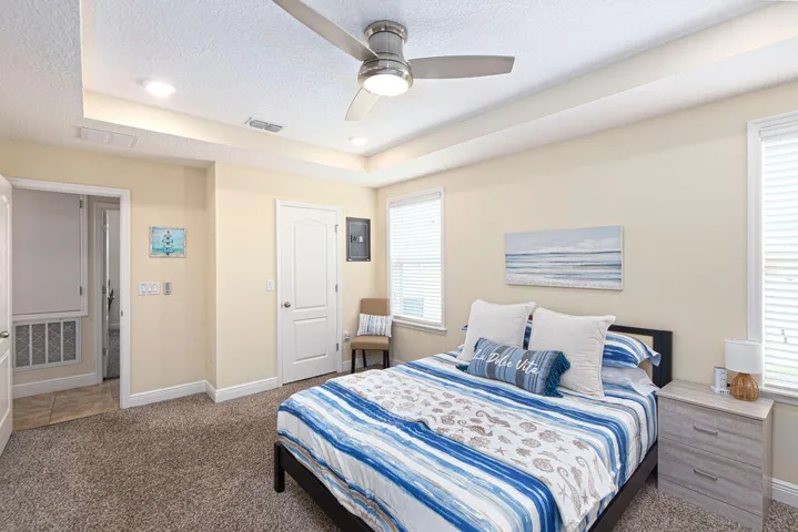 Primary bedroom with tray ceiling, ceiling fan, carpet and access to the en-suite bath