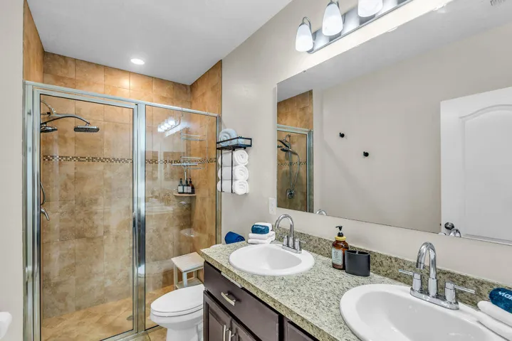 Primary bath with glass-enclosed walk-in tiled shower, double vanity with granite countertop