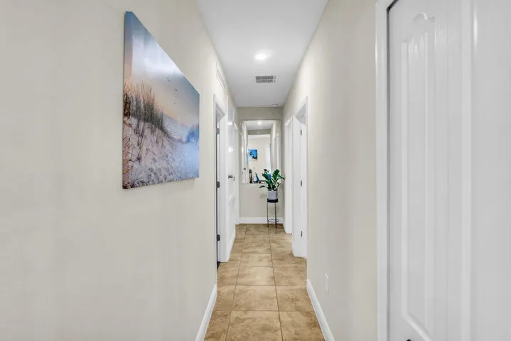 Recessed lighting illuminates a hallway with tile flooring and white trim