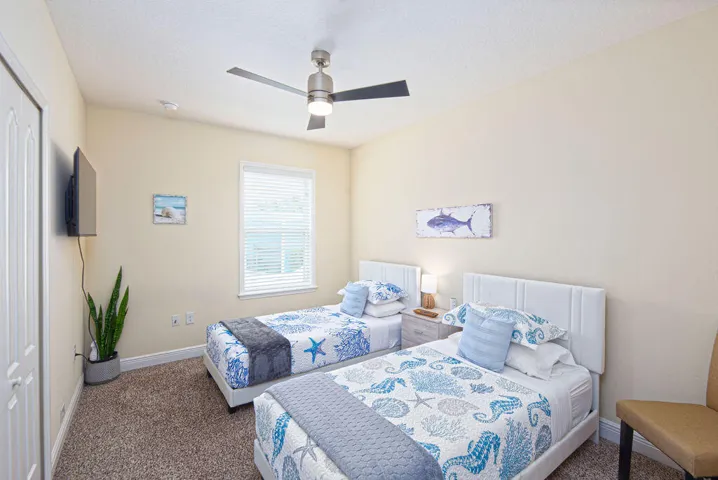 Guest bedroom with two beds, ceiling fan, carpet and natural light