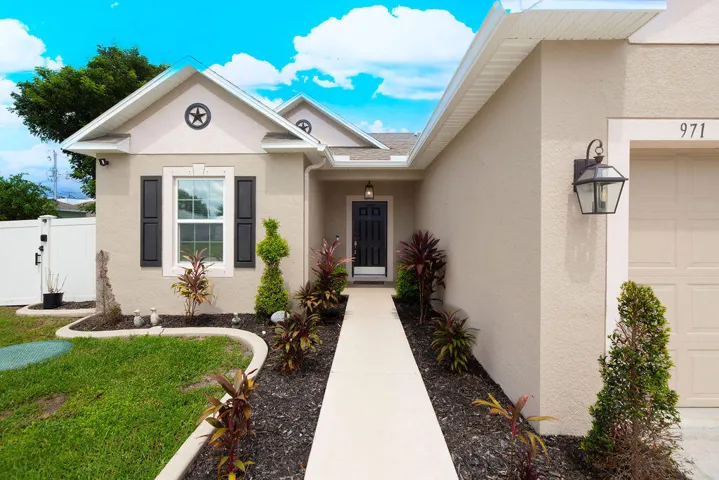 Stucco exterior with decorative window shutters, a paved walkway, exterior light fixtures, and manicured landscaping
