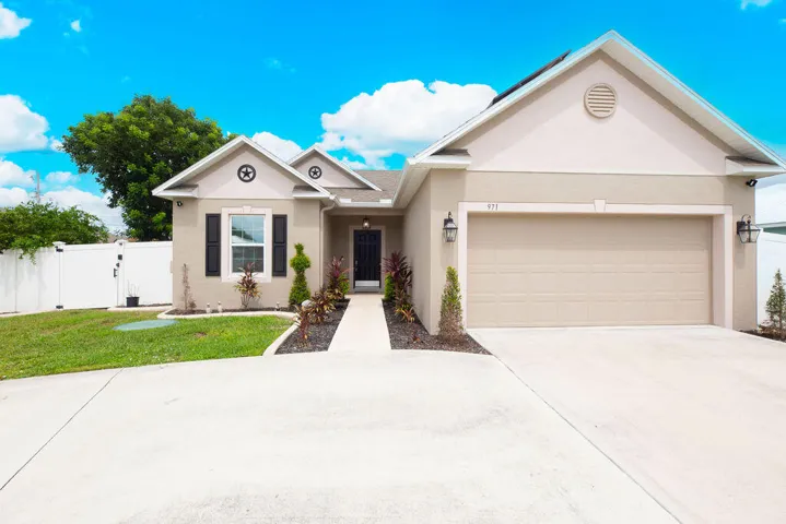 Stucco exterior with a gable roof, attached two-car garage, concrete driveway, and a white privacy fence