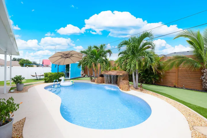 Heated gunite pool with rock waterfall, turf and tropical landscaping