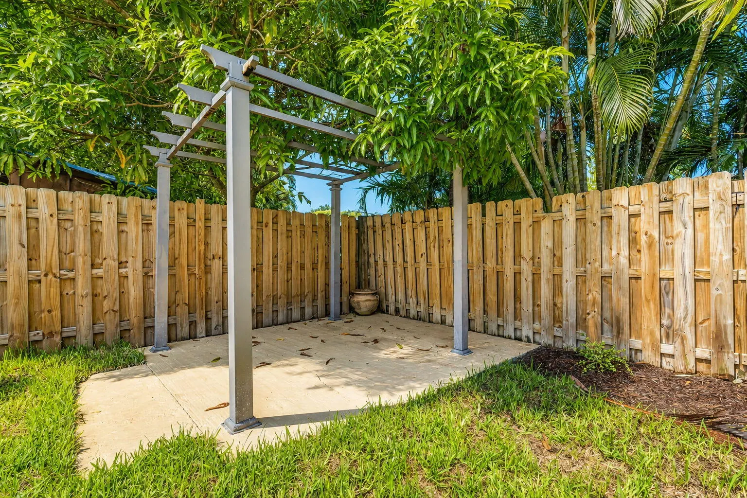 Private backyard featuring a concrete patio with a metal pergola, wood privacy fencing, and established trees