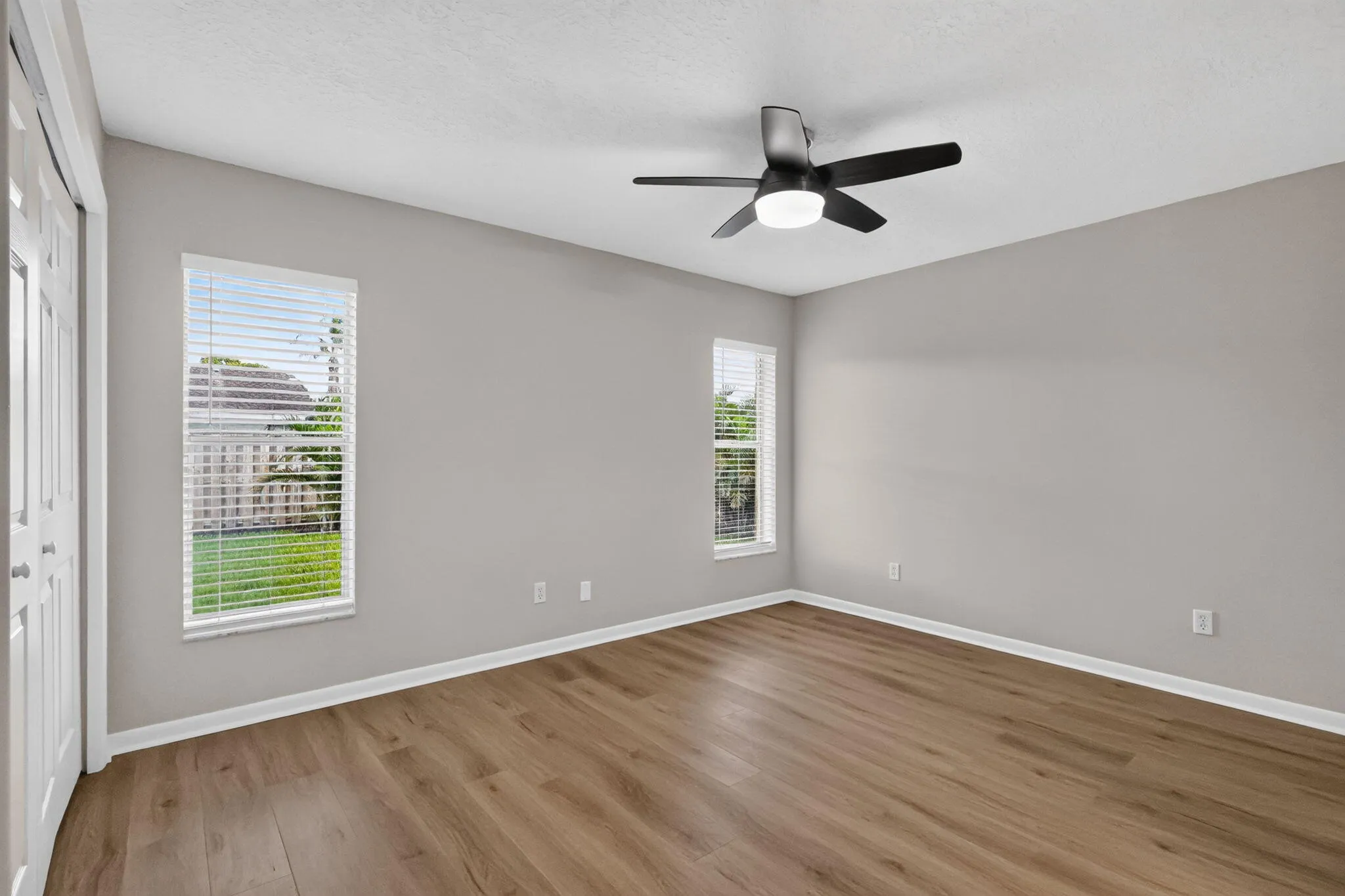 Wood-finish flooring, neutral wall tones, two windows with blinds, and a ceiling fan with integrated lighting