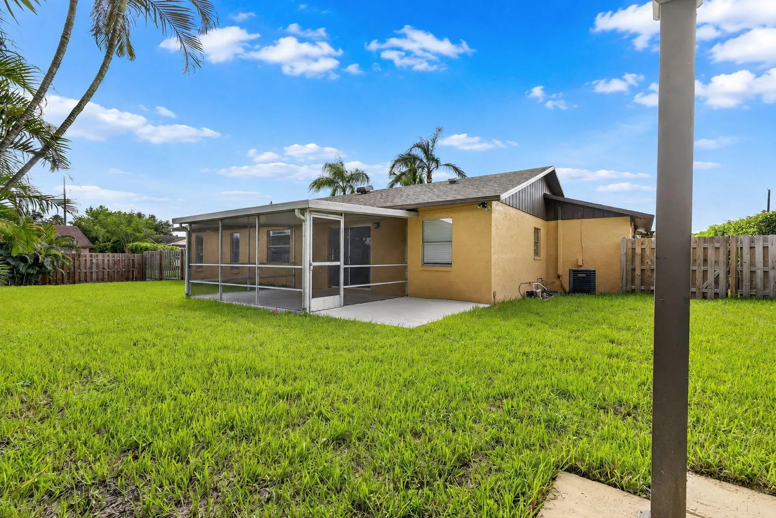 Expansive green lawn with a screened-in patio and concrete slab, featuring a privacy fence and mature palm trees