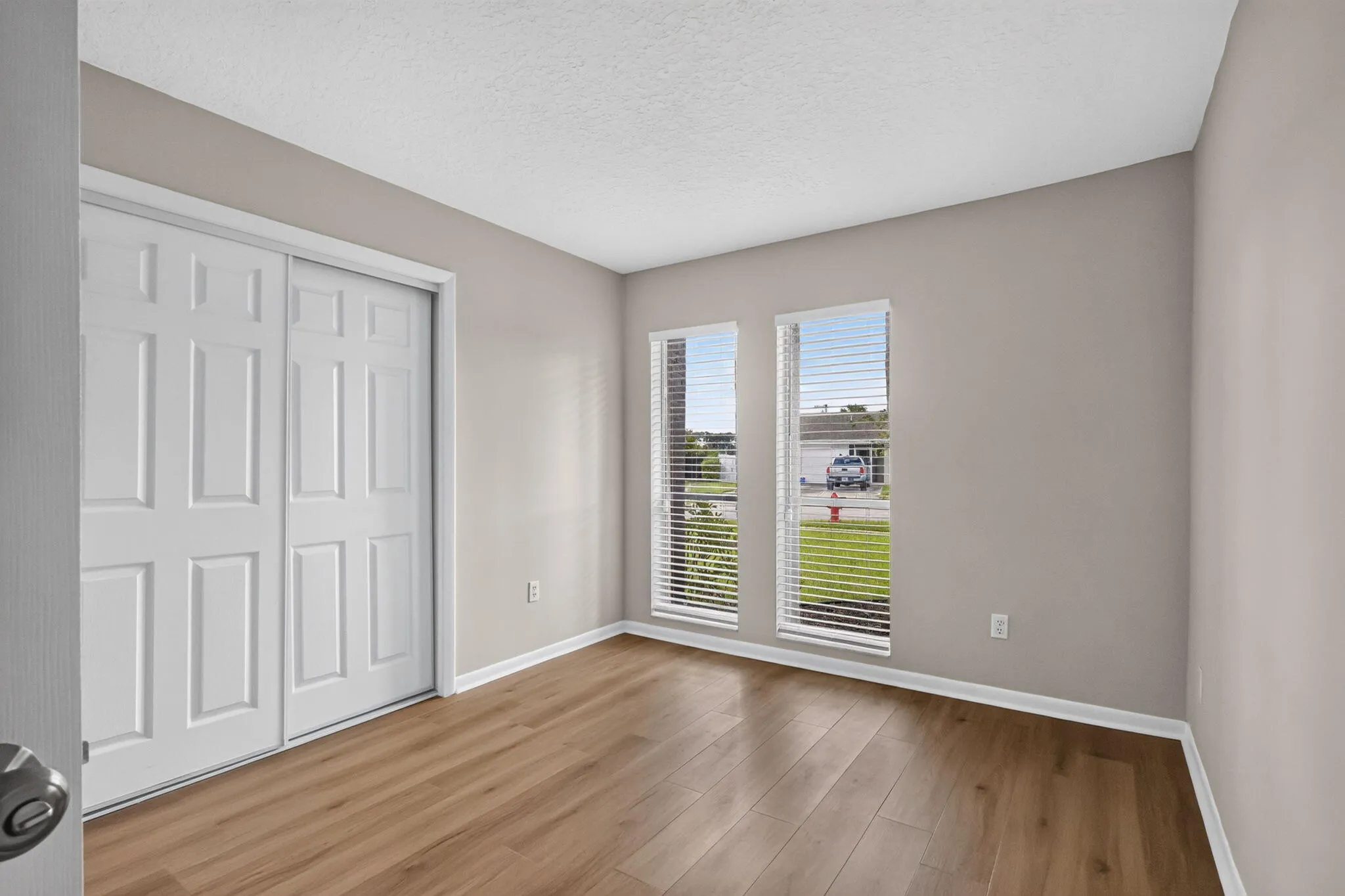 Wood-finish flooring, two window openings, neutral wall paint, white trim, and a white bi-fold closet