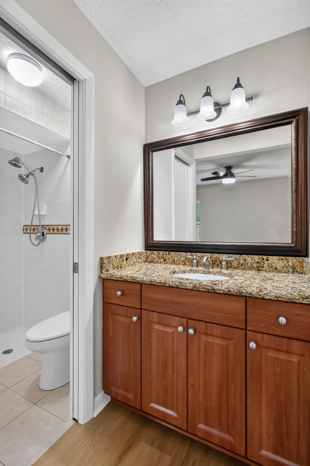 Wood-finish flooring leading to a vanity with a stone countertop, an integrated sink, and wood cabinetry