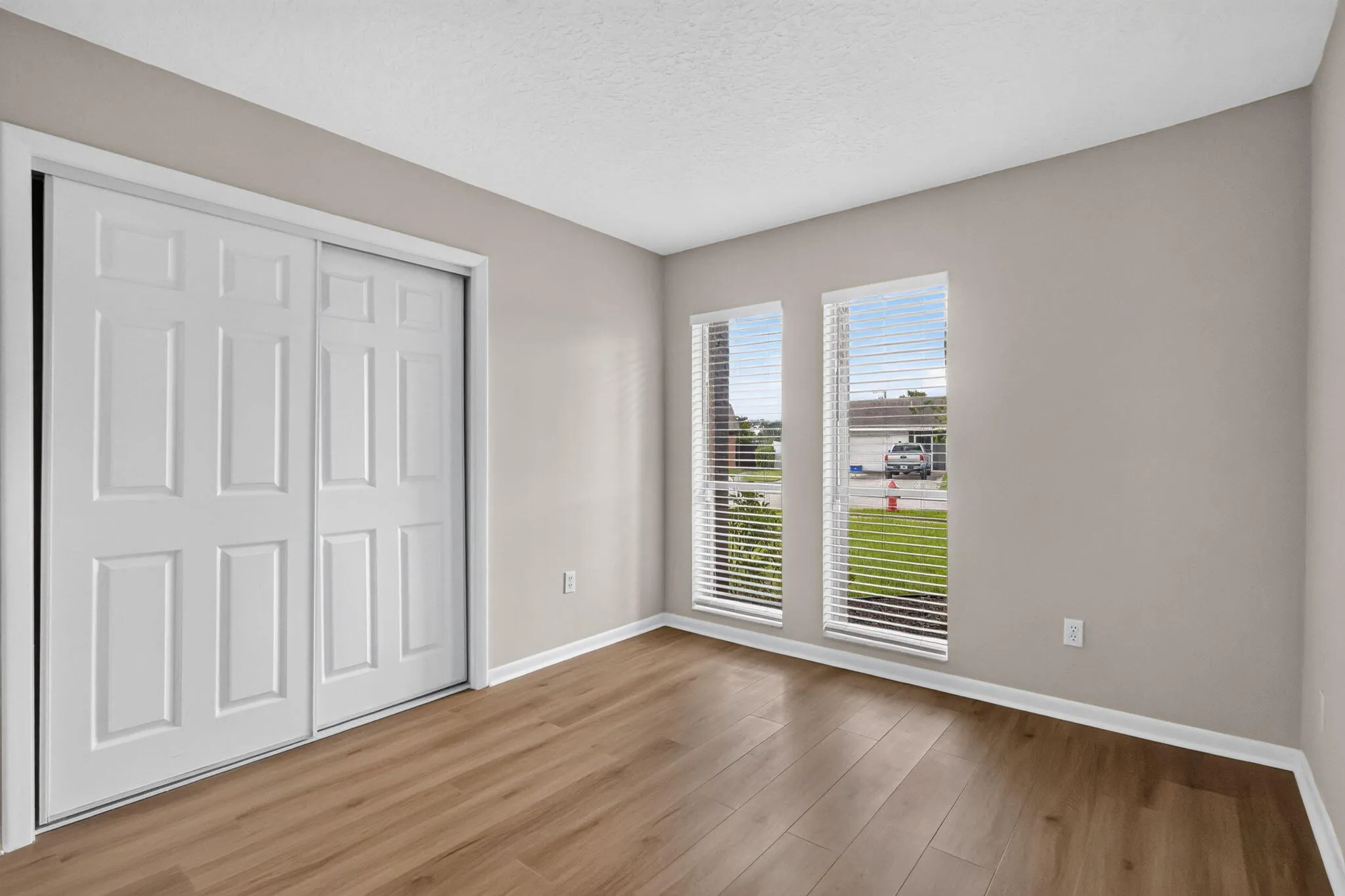 Wood-finish flooring, two vertical windows with blinds, white trim, and a bi-fold closet door