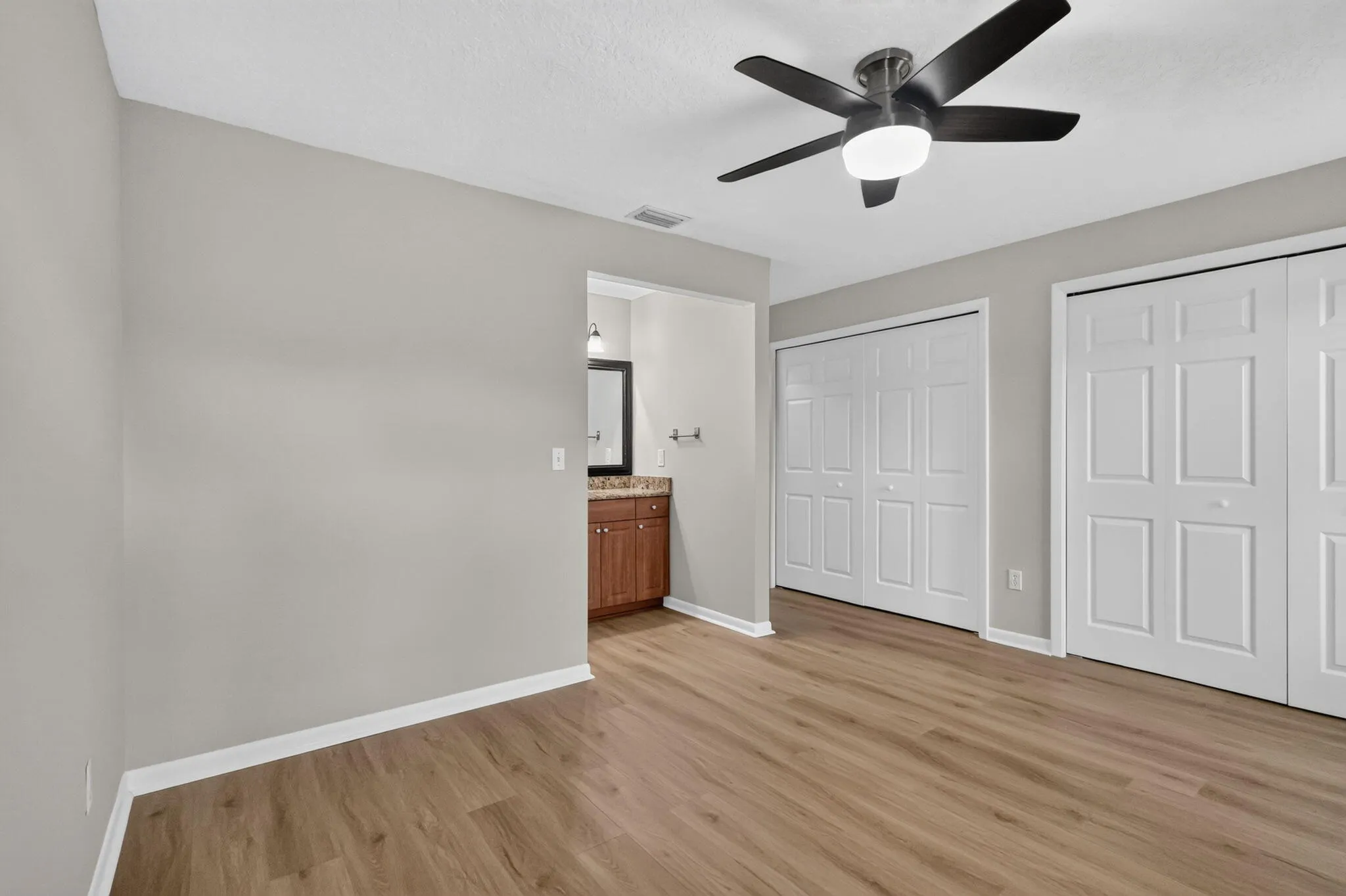 Wood-finish flooring, ceiling fan with integrated lighting, bi-fold closet doors, and an en-suite vanity with a mirrored cabinet