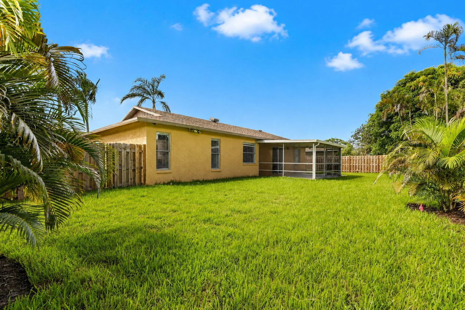 Expansive backyard with a manicured lawn, a full wooden privacy fence, and a screened-in patio