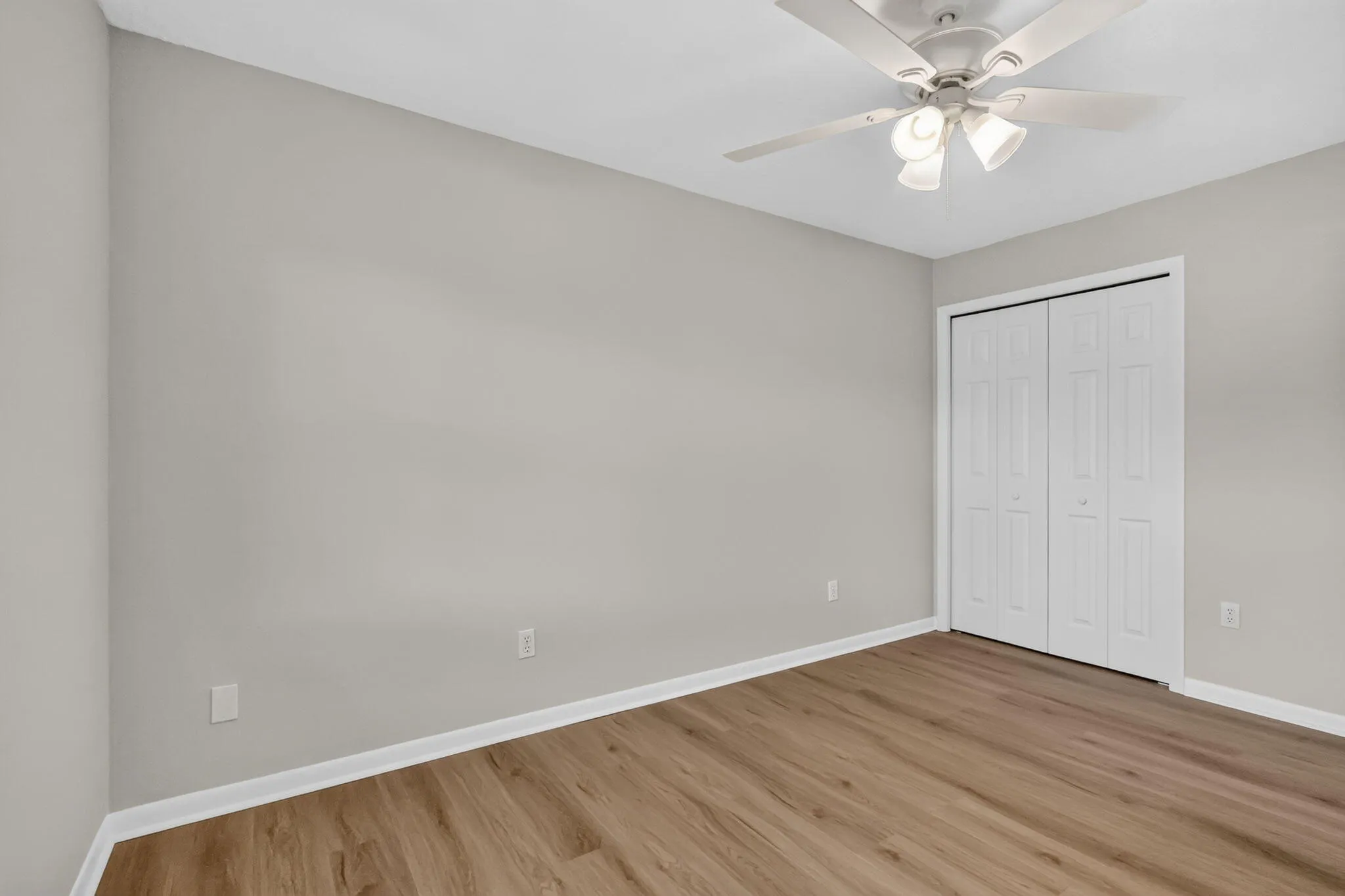 Wood-finish flooring, light gray walls, white trim, bi-fold closet doors, and a ceiling fan with integrated lighting