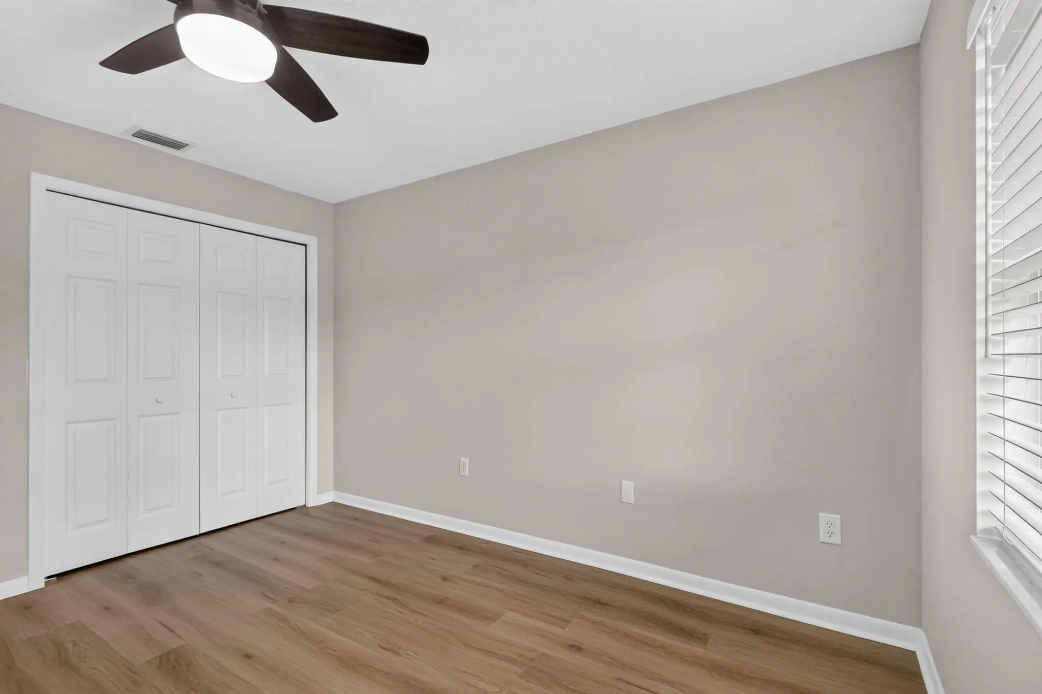 Wood-finish flooring with light-toned walls, white bi-fold closet doors, and a ceiling fan with integrated lighting
