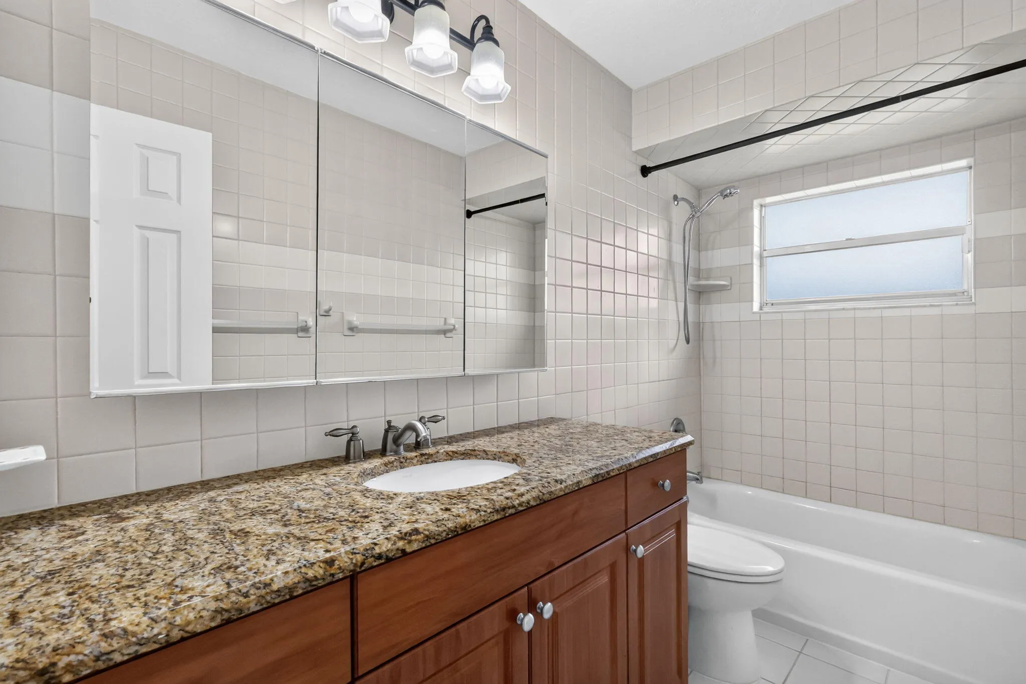Spacious bathroom featuring a wood-finish vanity with granite countertop, integrated sink, and a mirrored medicine cabinet