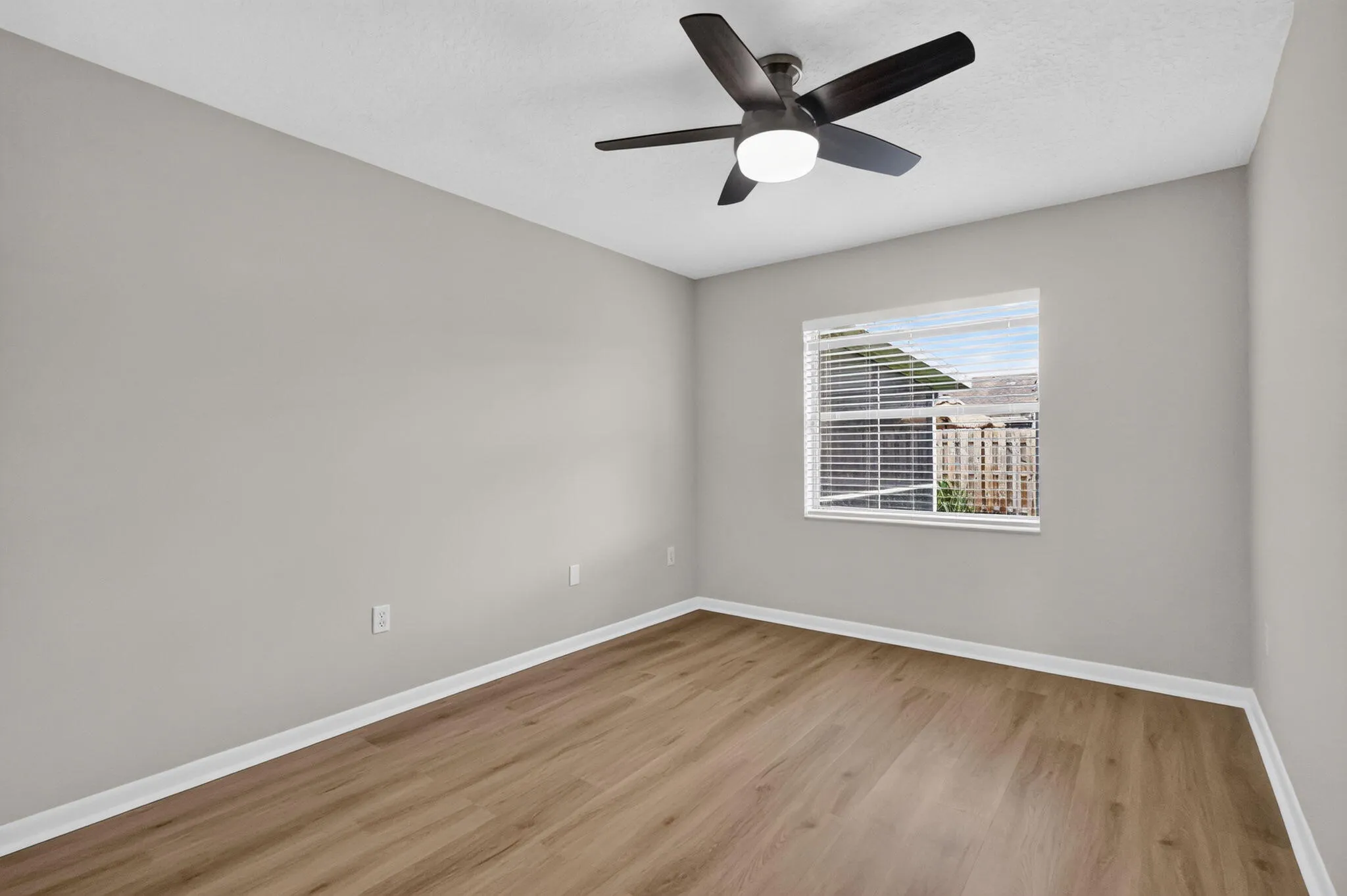 Recessed window with horizontal blinds, overhead ceiling fan with integrated lighting, wood-finish flooring, and light-toned wall finishes