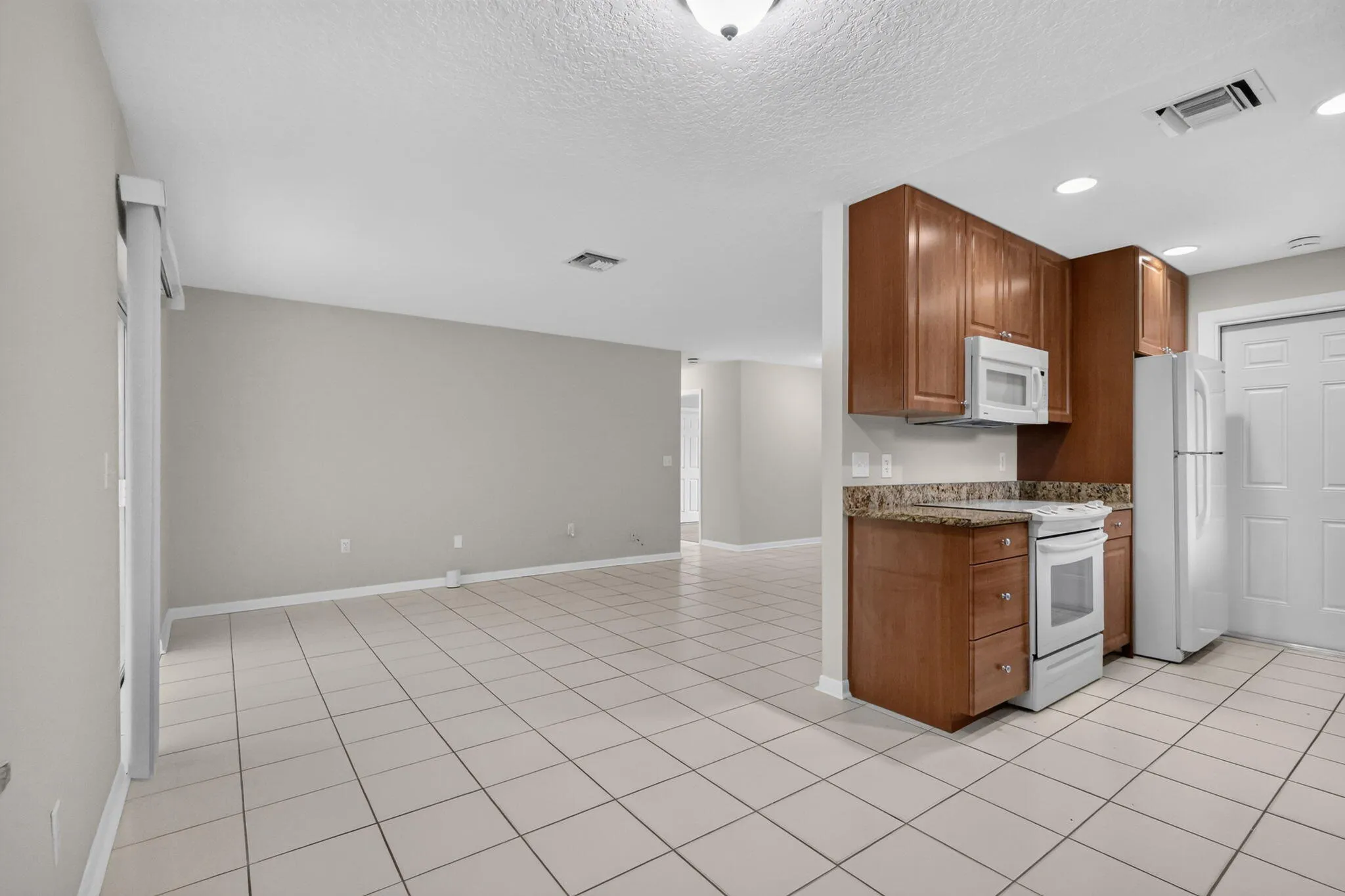 Kitchen area featuring wood-finish cabinetry, white appliances, and a stone-finish countertop