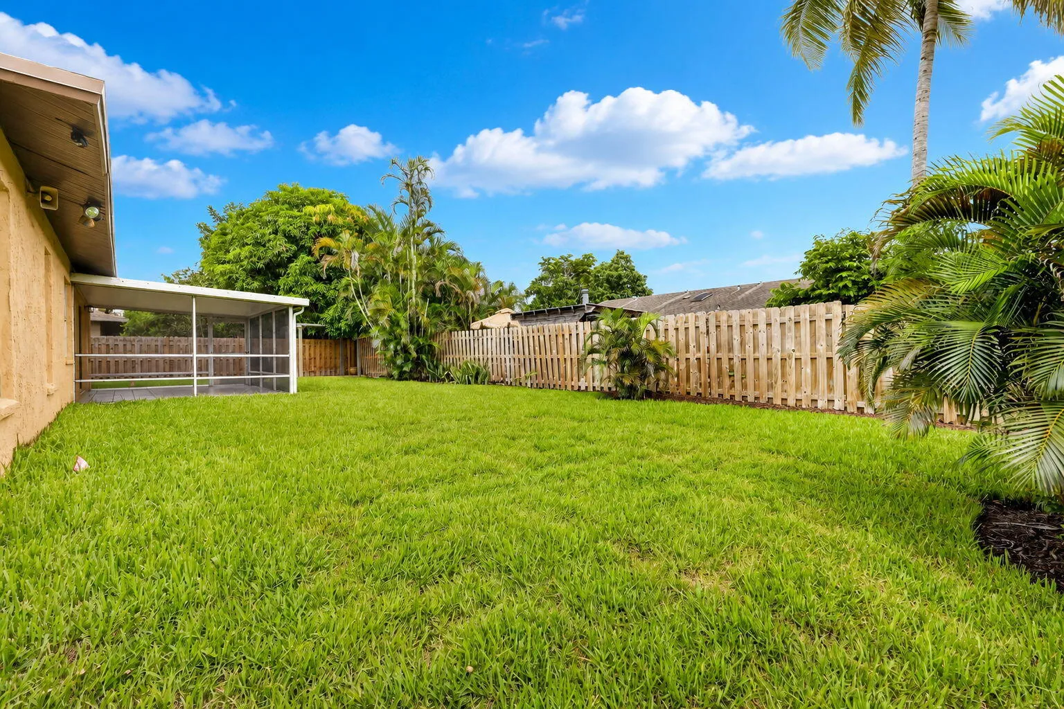 Expansive backyard featuring a green lawn, wood privacy fencing, and mature tropical landscaping