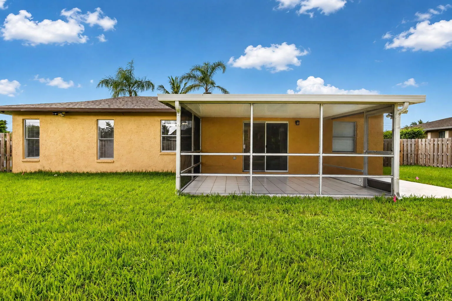 Expansive lawn featuring a screened-in patio, sliding glass door access, stucco exterior, and privacy fencing
