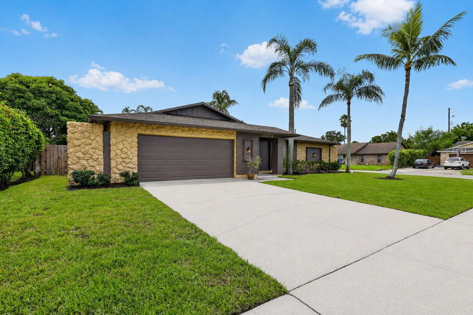 Single-story residence featuring a two-car garage, stone-finish exterior accents, a concrete driveway, and mature palm trees