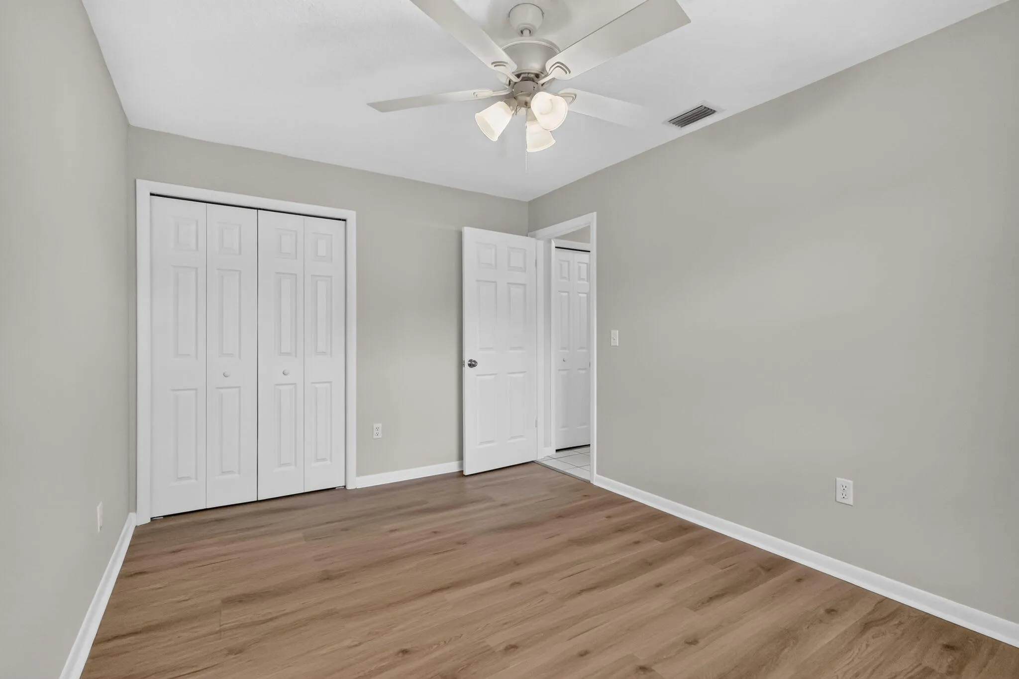 Wood-finish flooring, light gray wall tones, and a white ceiling fan with integrated lighting