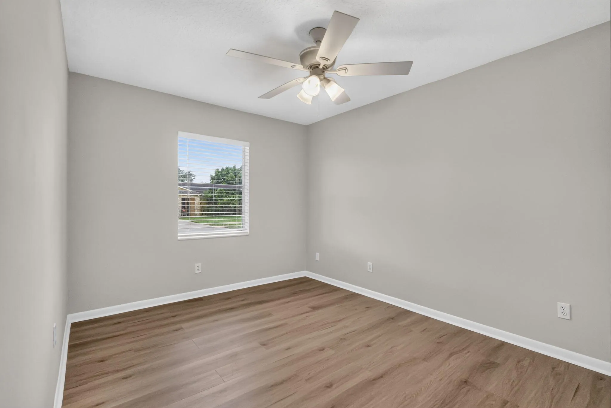 Wood-finish flooring, light grey walls, white trim, window with blinds, ceiling fan with integrated lighting