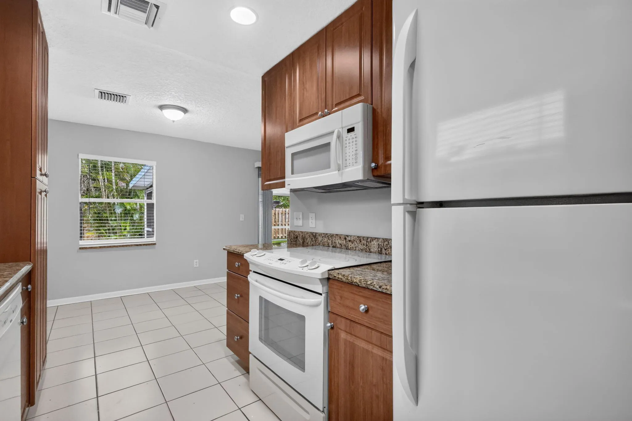 Kitchen featuring wood cabinetry, white appliances, recessed lighting, and tile flooring