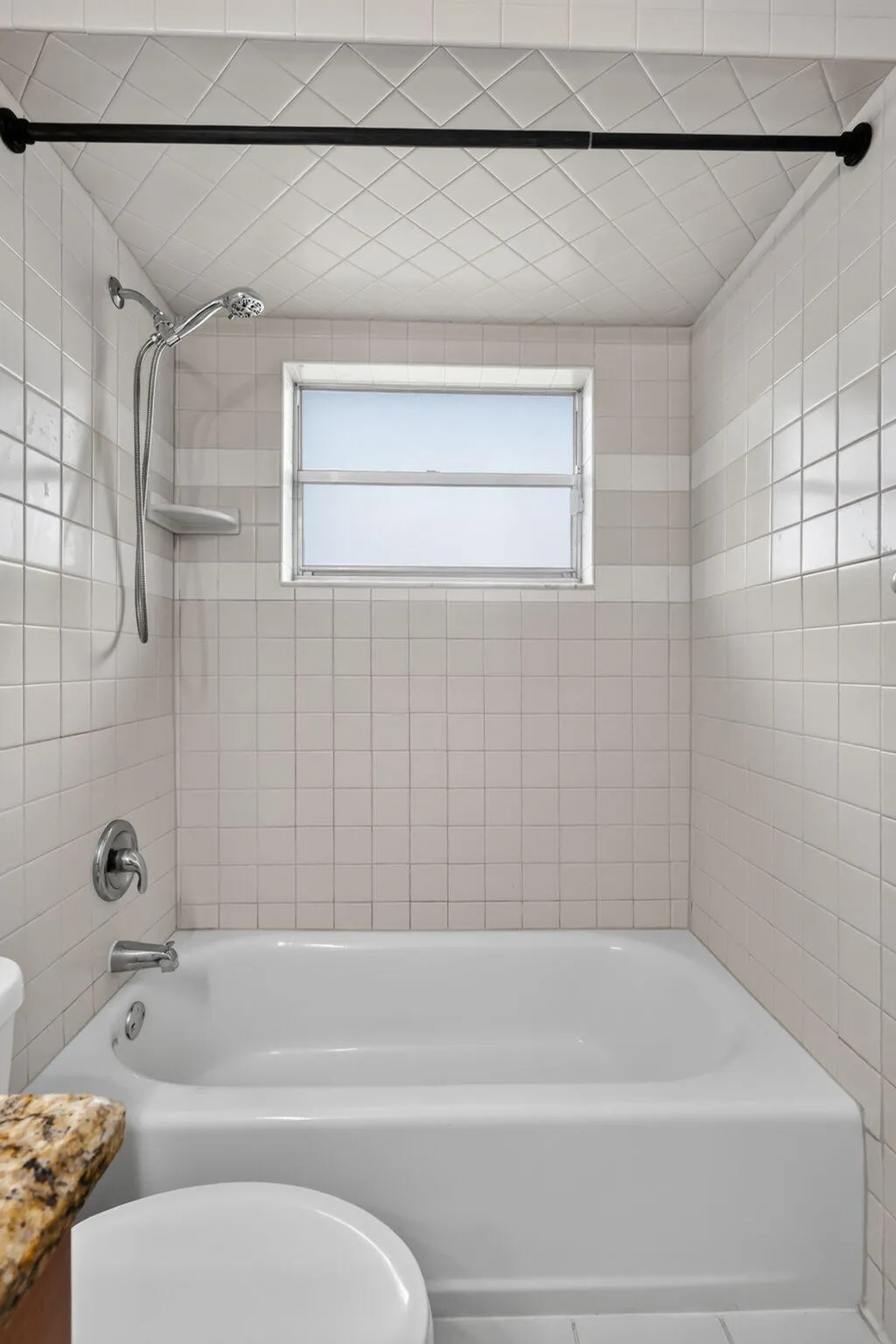 Bathtub with a shower fixture, wall-mounted shower head, and tiled surround