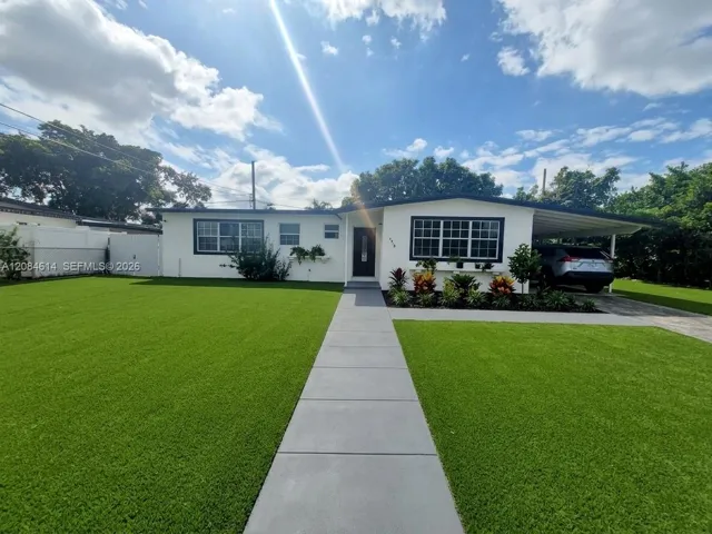 Single-story exterior featuring white stucco siding, a concrete walkway, a carport, and low-maintenance turf lawn