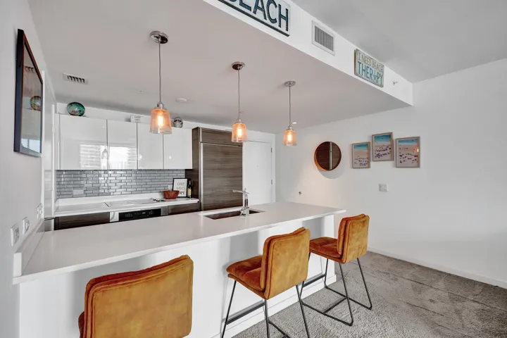 Kitchen featuring white countertop, subway tile backsplash, white upper cabinetry, integrated refrigerator, and pendant lighting