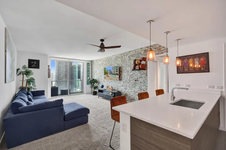Open concept living space featuring a textured accent wall, integrated kitchen island with a single-basin sink, pendant lighting, and a ceiling fan