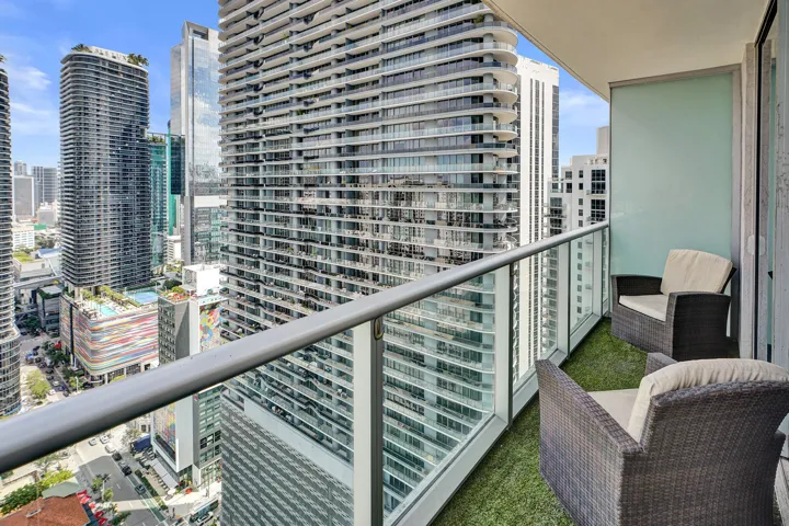 Balcony with glass railing, turf-covered flooring, and surrounding cityscape
