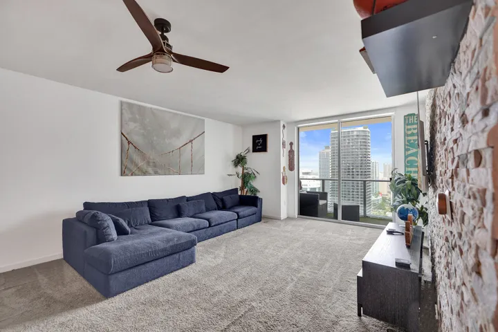 Full-height glass doors providing abundant light, ceiling fan with integrated lighting, textured accent wall, and wall-to-wall carpeting